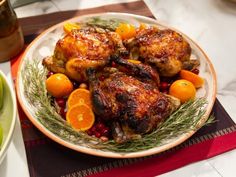 a white plate topped with chicken and oranges next to a bowl of fruit on a table