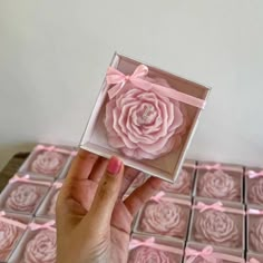 a hand holding up a pink rose in a box with chocolates on the side