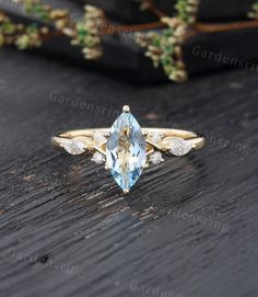 an aqua blue topazte and diamond ring on a wooden table with greenery in the background