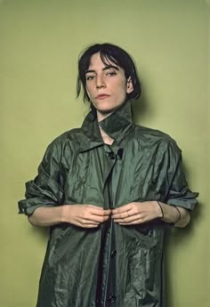 a woman standing in front of a green wall with her hands on her hips and looking at the camera