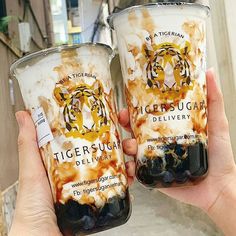 two people holding up cups with tiger sugar on them