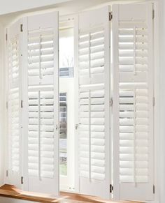 an open window with white shutters and wood flooring