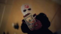 a person holding up a dollar bill in front of a white mask on the wall