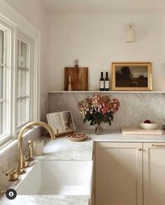 a white kitchen with marble counter tops and gold faucet, an open window over the sink