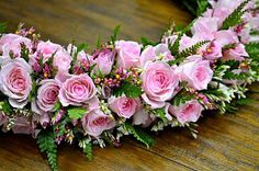 pink roses and greenery are arranged on a wooden table for a floral arrangement in the shape of a wreath