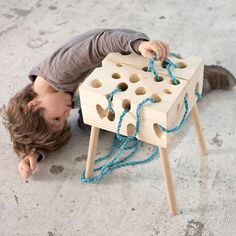 a young boy playing with a wooden block and string toy on the floor in front of him