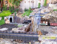 a model train track with a waterfall coming out of the tunnel and cars on it