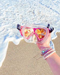 a person wearing goggles and holding up a shell in front of the ocean water