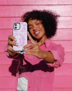 a woman taking a selfie with her cell phone in front of a pink wall