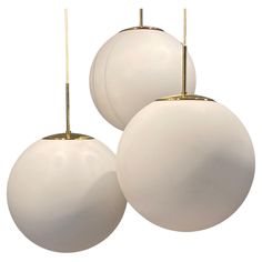 three white balls are hanging from brass poles on a white background, with one light turned off and the other turned off