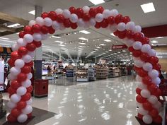 an archway made out of red and white balloons in a shopping center with people walking by