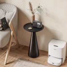 a small black table next to a chair and a printer on a wooden floor in front of a beige wall