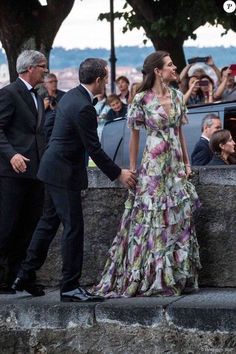 a man and woman in formal wear standing next to each other with people taking pictures behind them