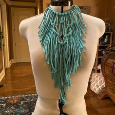 a white mannequin with a blue scarf on it's neck and fringes