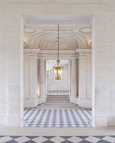 an empty hallway with blue and white checkered flooring, chandelier hanging from the ceiling