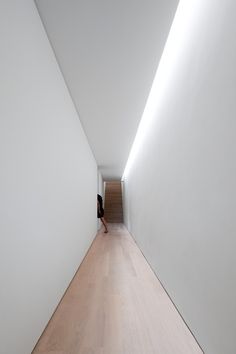 a person walking down a long hallway with white walls and wood flooring on both sides