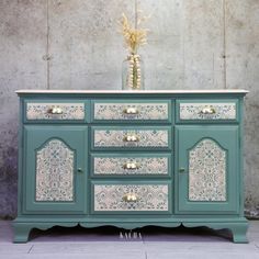 an old dresser painted in green and white with gold hardware on the top, next to a vase filled with flowers