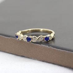 a yellow gold ring with blue stones and diamonds on top of a black box next to a book