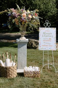 a sign that is sitting in the grass next to some umbrellas and baskets with flowers