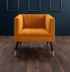 an orange chair sitting on top of a wooden floor next to a blue wall and black framed pictures