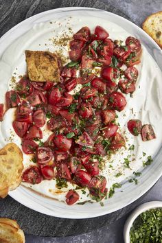 a white plate topped with sliced tomatoes and toasted bread next to a bowl of pesto