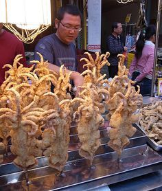 a man standing in front of a counter filled with fried food and other foods on trays