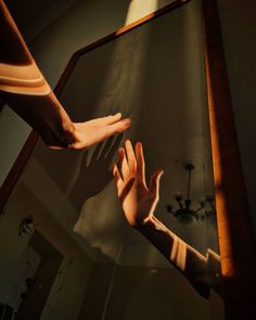 two hands reaching for each other in front of a mirror with light coming through it