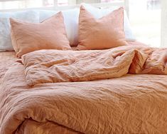 an unmade bed with peach colored linens and pillows