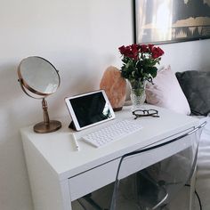 a laptop computer sitting on top of a white desk next to a vase with flowers