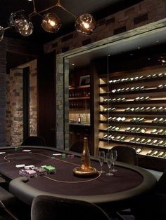 a poker table in a room with wine bottles on the wall and lights hanging from the ceiling