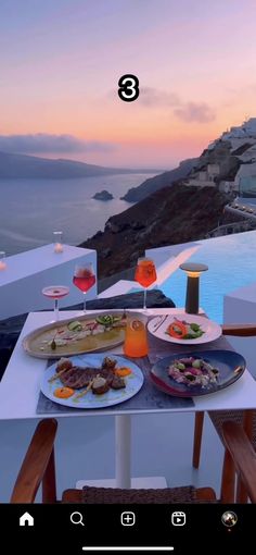 a table with food and drinks on it next to the ocean at sunset or sunrise