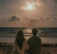 two people sitting on the beach watching the moon