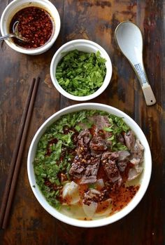 two bowls filled with meat and vegetables next to chopsticks on a wooden table