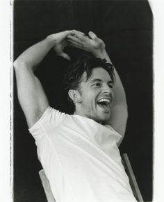 a black and white photo of a man smiling with his hands on his head,