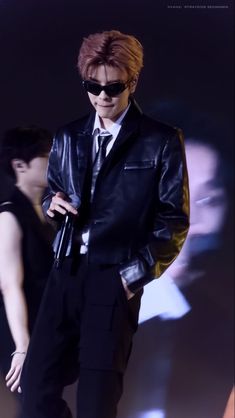 a male in a black leather jacket and sunglasses is standing with his hands on his hips