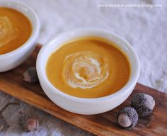 two white bowls filled with soup on top of a wooden board