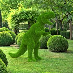 a dinosaur made out of grass in the middle of some bushes