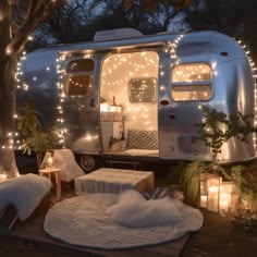 an airstream is lit up with christmas lights and blankets on the ground in front of it