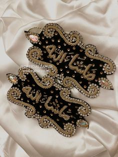 two black and gold brooches sitting on top of a white satin material sheet