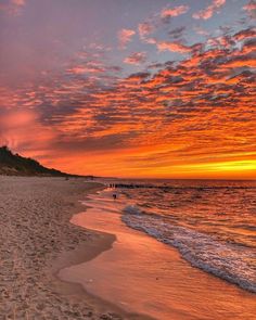 people are walking on the beach as the sun goes down in the sky over the water