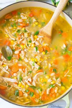 a pot filled with chicken and bean soup on top of a table next to a wooden spoon