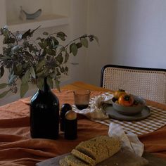 the table is set with bread, oranges and flowers in a glass vase on it