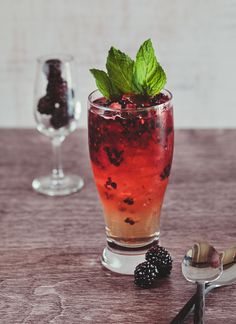 a glass filled with ice and blackberries on top of a table next to a spoon