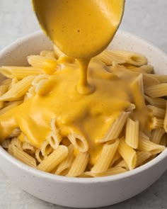 a white bowl filled with macaroni and cheese being drizzled over