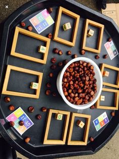 a bowl of nuts is surrounded by wooden squares and magnets on a black table