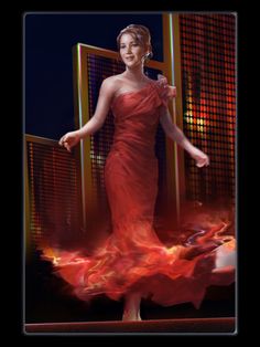 a woman in a red dress is standing on a stage with fire behind her,