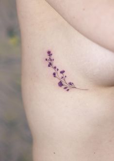 a small tattoo on the side of a woman's stomach that has purple flowers growing out of it