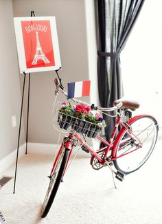 a red bicycle with flowers in the basket next to a sign that says bonjouie