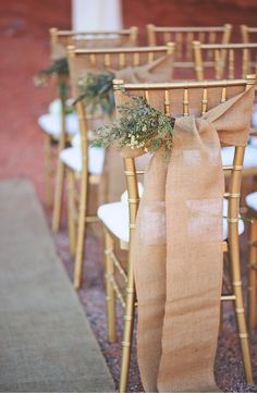 the chairs are lined up with burlocks and greenery tied to each chair