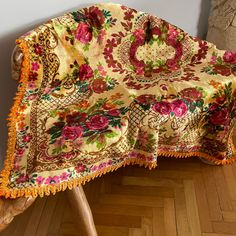 a floral blanket on a wooden bench in a room with hard wood flooring and white walls